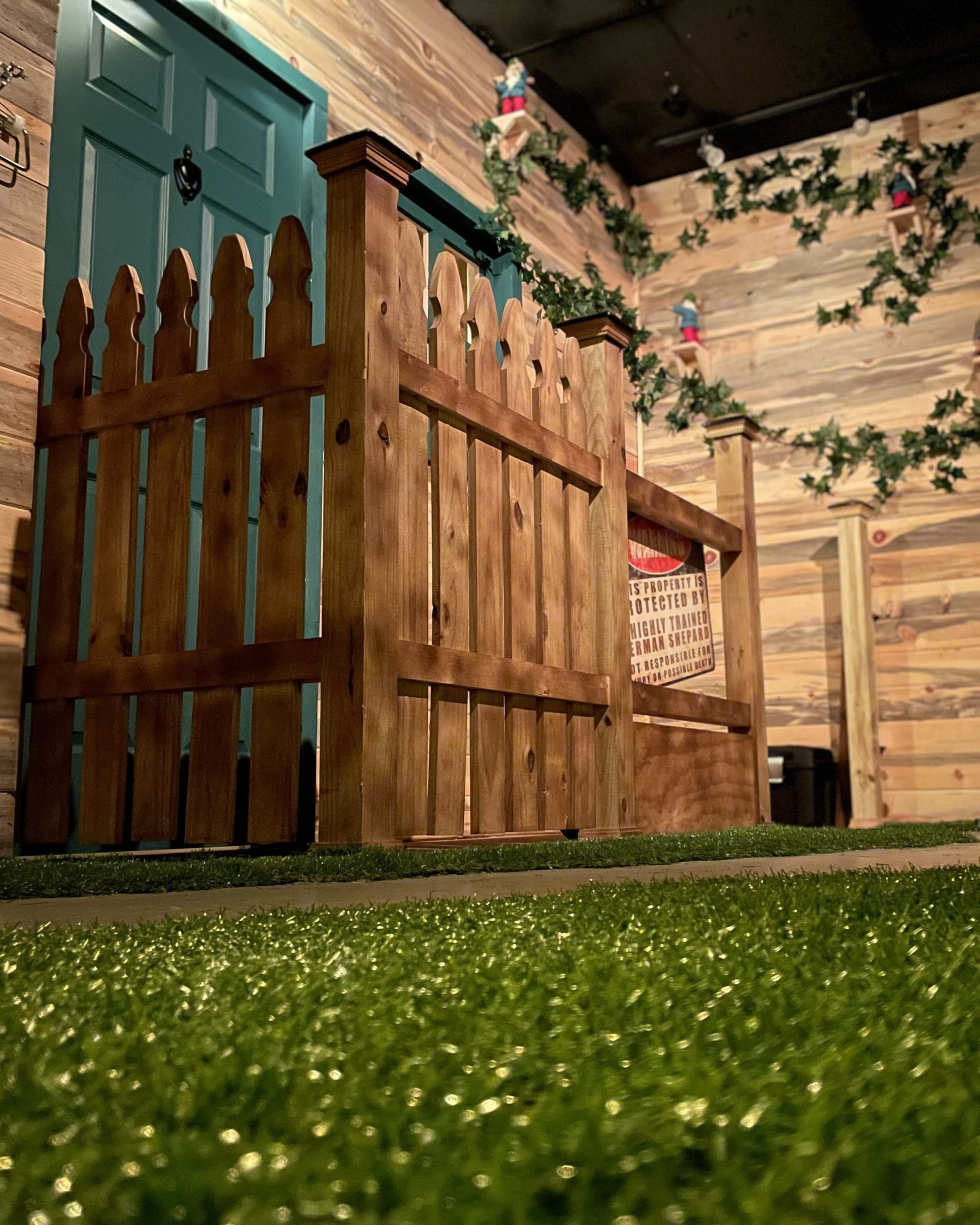 Escape room set built as a backyard with a picket fence, teal door and ivy-covered wall